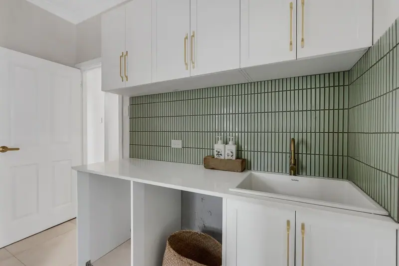 Laundry renovation with green finger tiles, white cabinetry and brass fittings